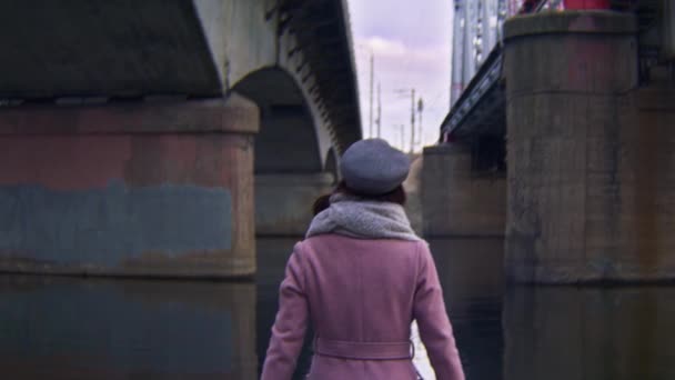 Kvinnan går i vattnet under broar. Lagerbilder. Bakifrån av attraktiv ung kvinna promenader under gamla broar på hösten — Stockvideo