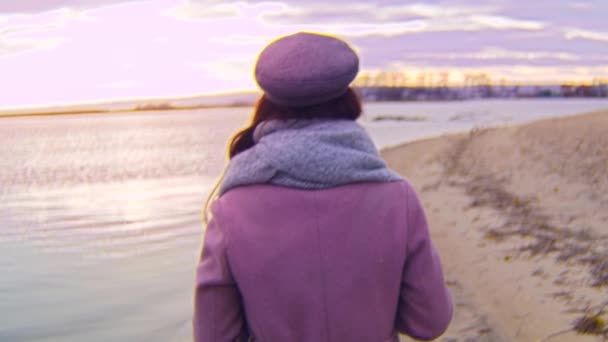 Tylny widok atrakcyjnej kobiety spacerującej na tle zachodzącego słońca krajobrazu wybrzeża. Materiał filmowy. Piękny nadmorski krajobraz w kolorach zachodu słońca i młoda kobieta spacerująca po plaży jesienią — Wideo stockowe