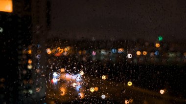 Pencerenin arkasında, üzerinde su damlaları olan büyük bir şehrin güzel odaksız parlak ışıkları. Kavram. Cam pencereye yağmur damlaları ve bulanık bokeh arkaplan.