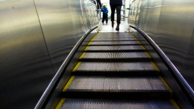 Yeraltı istasyonundan merdivenlere kadar yürüyen metal merdiven, toplu taşıma. Kavram. Bir adam, bir kadın ve bir çocuğun metroda yürüyen merdivene binişi..