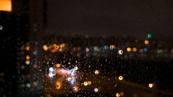 Piękne rozproszone jasne światła dużego miasta za oknem z kroplami wody. Koncepcja. Krople deszczu na szklane okno i rozmyte tło bokeh. — Zdjęcie stockowe