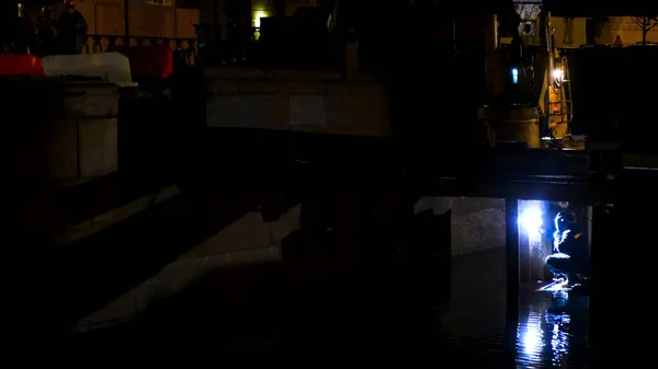 Reconstruction d'un pont sur la rivière la nuit dans la ville. Concept. Un homme travailleur dans des poutres de soudure uniformes de protection pour un pont marchant . — Photo