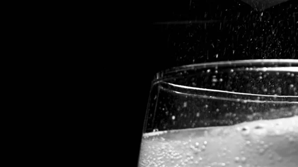 Glass with hissing carbonated bubbles. Stock footage. Close-up of carbonated foam bubbling and sizzling formed to edge of glass on black isolated background — Stock Photo, Image