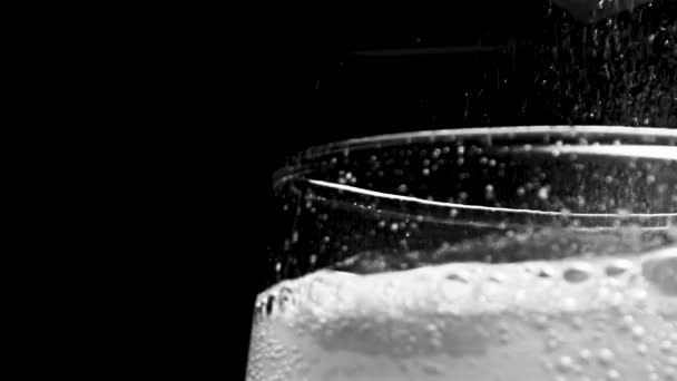 Glass with hissing carbonated bubbles. Stock footage. Close-up of carbonated foam bubbling and sizzling formed to edge of glass on black isolated background — Stock Video