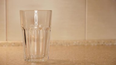 Suyun yakın çekimi şeffaf camlara döküldü. Kavram. Temiz kaynamış su, eski mutfak fayanslarının arka planındaki şeffaf camlara dökülüyor.