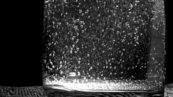 Close-up of sparkling water with bubbles in glass. Stock footage. Many bubbles rise from bottom of clear glass of sparkling water on black background — 비디오