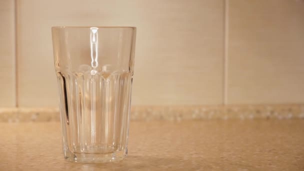 Gros plan de l'eau versée dans du verre transparent à facettes. Concept. L'eau bouillie propre est versée dans du verre transparent sur le fond de l'ancien mur de tuiles de cuisine 