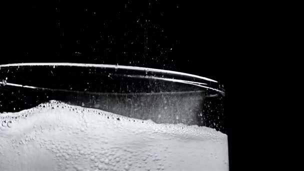 Glass with hissing carbonated bubbles. Stock footage. Close-up of carbonated foam bubbling and sizzling formed to edge of glass on black isolated background — 비디오