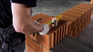 Havan ve tuğlalardan duvar yapan bir endüstriyel işçiyi çekiç ve seviye aleti kullanarak kapatın. Stok görüntüleri. Erkek eller dış duvarları inşa ediyor, betona tuğla döşemek için çekiç kullanıyor..