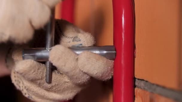 Στενή θέα ενός αρσενικού εργάτη που χρησιμοποιεί γαλλικό κλειδί για εργασίες τοίχου. Στικ. Master προσπαθεί να προσαρτήσει μεταλλική λεπτομέρεια στον κόκκινο τοίχο τούβλο. — Αρχείο Βίντεο