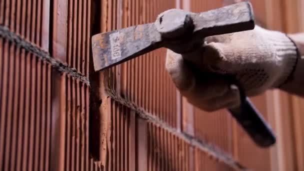Close-up van een man die de muur van keramische blokken op de bouwplaats hamert. Voorraadbeelden. Werknemer in beschermende handschoenen maakt een gat in de muur. — Stockvideo
