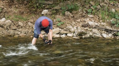 Kayalık bir nehirde kameralı bir adam su yüzeyinin fotoğraflarını çekiyor. Stok görüntüleri. Elinde kamerayla orman deresinin videolarını çeken bir erkek yürüyüşçü..