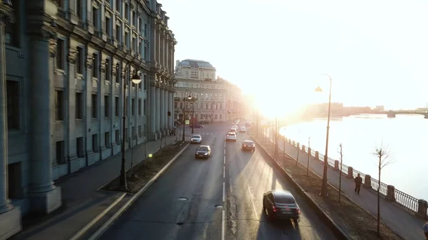 Utsikt över stadens gata med bilar och människor i med det ljusa ljuset av solnedgången i bakgrunden. Lagerbilder. Flygfoto av vackra byggnader nära floden, arkitektur koncept. — Stockfoto