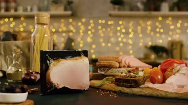 Tisch mit Fleisch-Snacks auf Girlanden-Hintergrund. Archivmaterial. Nahaufnahme der Zutaten für die Festtafel in der Küche mit Girlanden im Hintergrund — Stockvideo