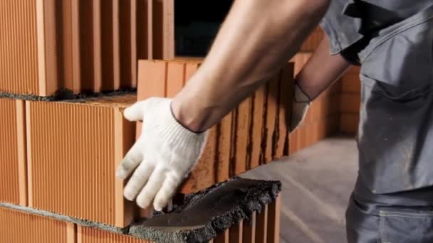 Albañil poniendo otra fila de ladrillos en el sitio de construcción. Imágenes de archivo. Acercamiento de un hombre con guantes protectores poniendo ladrillo pesado en el mortero . — Vídeo de stock