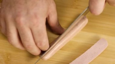 Sosis dilimleyen şefin yakın çekimi. Stok görüntüleri. Şef ahşap tahtada sulu pembe sosisli pizza dilimleri keser. Mutfakta, profesyonel yemek pişirme sürecinde.