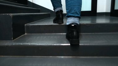 Merdivenlere tırmanırken yakın plan. Kavram. Deri çizmeler içinde güzel ayaklar ve kot pantolonlar odada merdivenleri tırmanır. Binada hızla merdivenleri çıkan kadın.