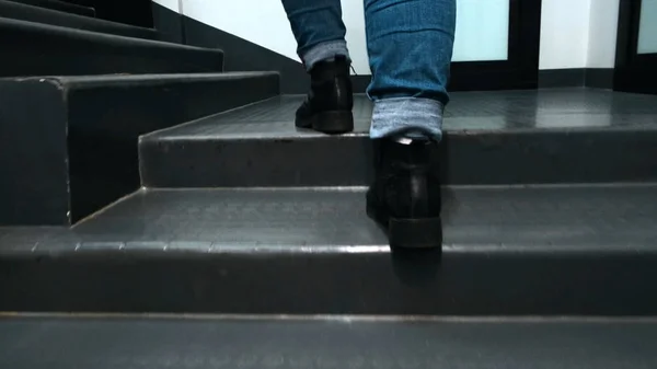 Close-up of feet climbing staircase. Concept. Beautiful feet in leather boots and jeans climb stairs in room. Woman quickly climbs stairs in building