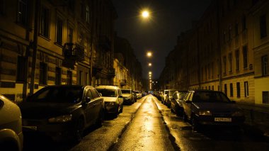 Geceleri park yerinde arabaları olan sarı fenerlerin ışığında Avrupa caddesi. Kavram. Geceleri sarı fenerlerle aydınlatılan park halindeki arabaları olan düz, güzel bir cadde.