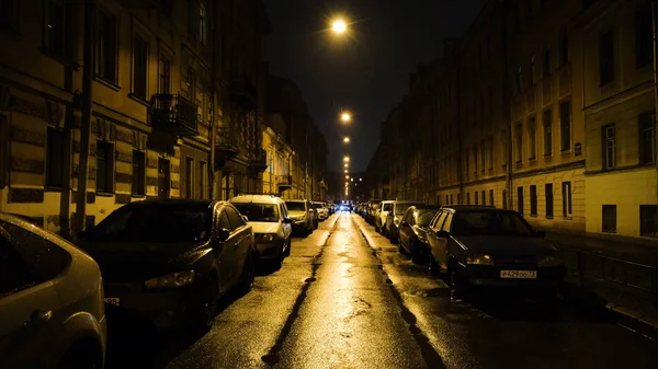 Europeisk gata i ljus av gula lyktor på natten med bilar i parkering. Begreppet. Rak vacker gata med bostadshus och parkerade bilar upplysta av gula lyktor på natten — Stockfoto
