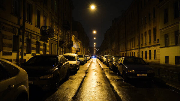 Европейская улица в свете желтых фонарей ночью с автомобилями на парковке. Концепция. Красивая улица с жилыми домами и припаркованными машинами, освещенными ночью желтыми фонарями
