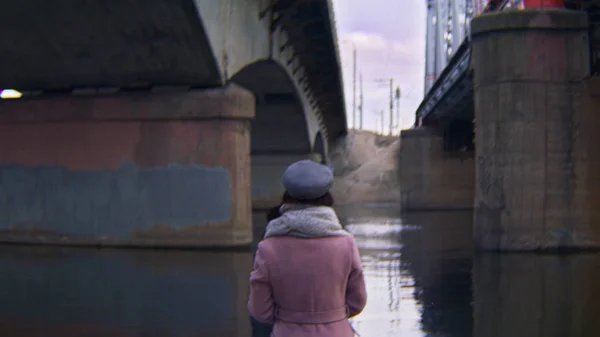 Femme marchant sur l'eau sous les ponts. Images d'archives. Vue arrière d'une jolie jeune femme marchant sous de vieux ponts en automne — Photo