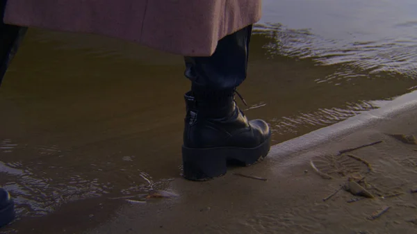 一个穿着鞋子在水上行走的女人的特写。库存录像。穿着黑色时髦皮鞋的女人晚上在沙滩上散步 — 图库照片