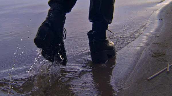 Close-up van een vrouw die in schoenen over water loopt. Voorraadbeelden. vrouw in zwart stijlvol lederen schoenen wandelingen op het water wandelen op het strand in de avond — Stockfoto