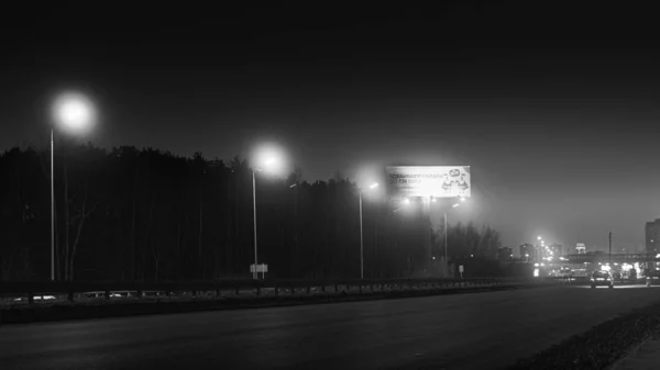 Vista em preto e branco do tráfego rodoviário da cidade à noite. Imagens de stock. Câmera limite de velocidade em preto e branco fica na auto-estrada na entrada da cidade à noite — Fotografia de Stock