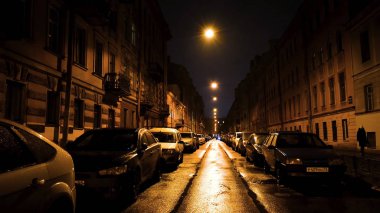 Büyük şehirde güzel bir gece ve sarı fenerlerin altındaki cadde. Kavram. Kaldırımda park etmiş bir sürü araba olan boş bir cadde..