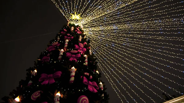 Dolní pohled na zelené vánoční stromeček top s girlandy a dekorativní hračky na noční černé obloze pozadí. Koncept. Novoroční smrk s barevnými stuhami a svíčkami. — Stock fotografie
