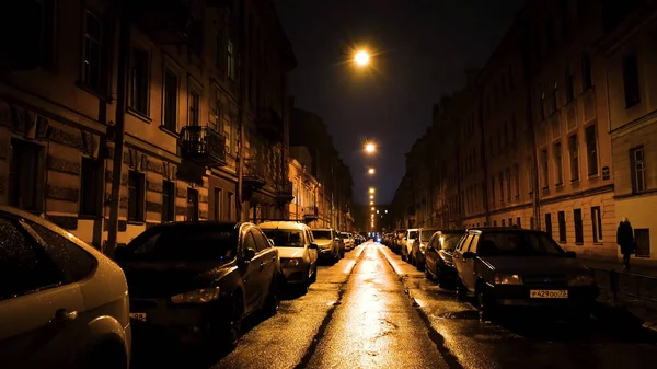 Vacker natt i storstaden och gatan under ljuset av gula lyktor. Begreppet. Tomma gatan med många parkerade bilar längs trottoaren. — Stockfoto