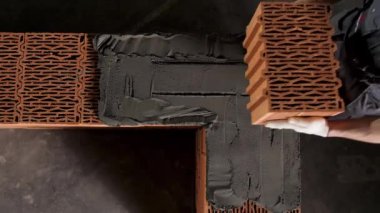 Bir adam tuğla bir duvar örüyor, tuğla bir ev inşa ediyor. Stok görüntüleri. Endüstriyel işçilerin çimento katmanına seramik blok yerleştirme görüntüsü.