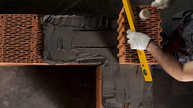 Top view of an industrial worker levelling ceramic brick wall with a wooden hammer. Stock footage. Building new wall of ceramic blocks. clipart