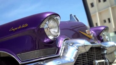 Gökyüzünün arka planında Retro Cadillac var. Aksiyon. Mor renkli lüks Cadillac ve gökyüzünün arka planında göz kamaştırıcı bir görünüş. Eski arabanın yeni hayatı. Amerikan otomobil klasiği