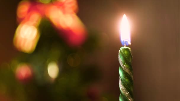 Candela accesa su uno sfondo sfocato colorato di Natale. Concetto. Primo piano della fiamma della candela verde di Capodanno posta di fronte all'abete rosso sfocato . — Video Stock