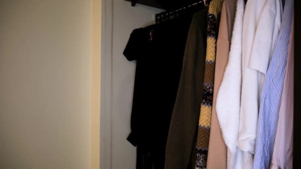 Крупним планом одяг у шафі біля білої стіни. Поняття. Вид збоку на різні сорочки в повній шафі, деталі інтер'єру квартири . — стокове відео