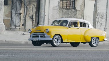 Havana, Küba - Mayıs 2019: Yabancılarla dolu eski sarı retro taksi. Başla. Yurtdışına seyahat eden turistler için Retro Car servis yapıyor. Turistler takside oturur ve ihtiyarların arka planına doğru yavaşça sürerler.