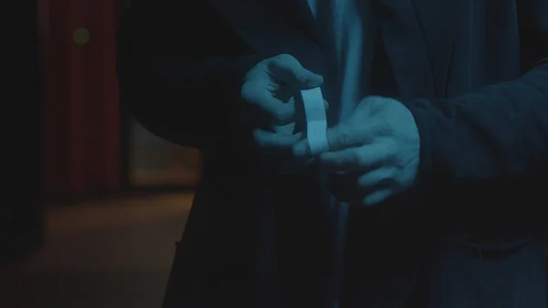 Κοντινό πλάνο του ανθρώπου που δένει τα δάχτυλά του. Στικ. Τα χέρια του είναι σφραγισμένα με γύψινα χέρια. Ληστής με παλτό βάζει γύψο στα δάχτυλά του πριν αγωνιστεί σε σκούρο φόντο του δρόμου — Φωτογραφία Αρχείου