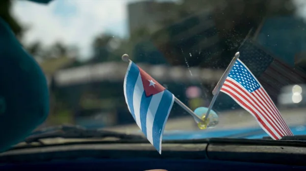 Close-up of flags of America and Cuba in car. Action. Beautiful flags adorn panel of retro car on background of road in hot country. Decoration for car — Stock Photo, Image