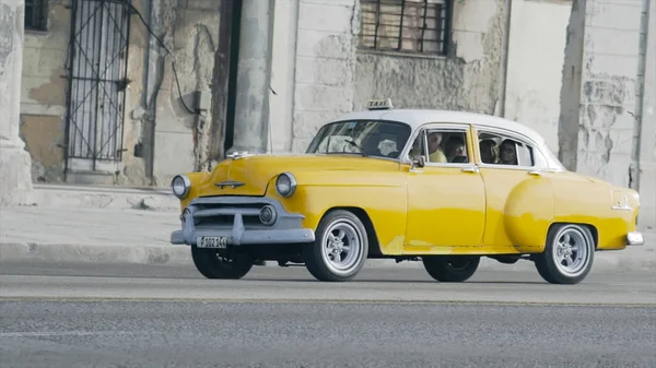 Havana, Küba - Mayıs 2019: Yabancılarla dolu eski sarı retro taksi. Başla. Yurtdışına seyahat eden turistler için Retro Car servis yapıyor. Turistler takside oturur ve ihtiyarların arka planına doğru yavaşça sürerler.