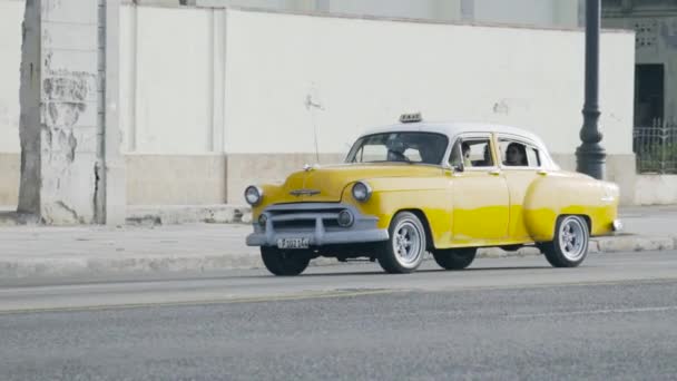 Гавана, Куба - май 2019 года: старое желтое ретро-такси с иностранцами. Начали. Ретро автомобиль, служащий такси для туристов, путешествующих за границей. Туристы садятся в такси, медленно проезжая на задний план старого разваливающегося — стоковое видео