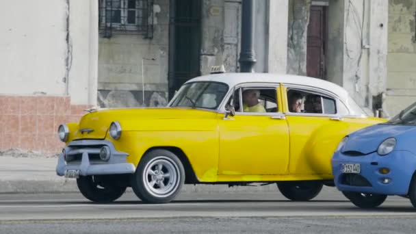 Гавана, Куба - май 2019 года: старое желтое ретро-такси с иностранцами. Начали. Ретро автомобиль, служащий такси для туристов, путешествующих за границей. Туристы садятся в такси, медленно проезжая на задний план старого разваливающегося — стоковое видео