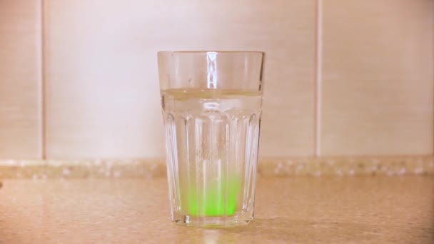 Primer plano de la tableta verde para preparar agua mineral casera en un vaso de agua colocado sobre la mesa contra la pared. Concepto. Bebida carbonatada con sabor a fruta . — Vídeo de stock