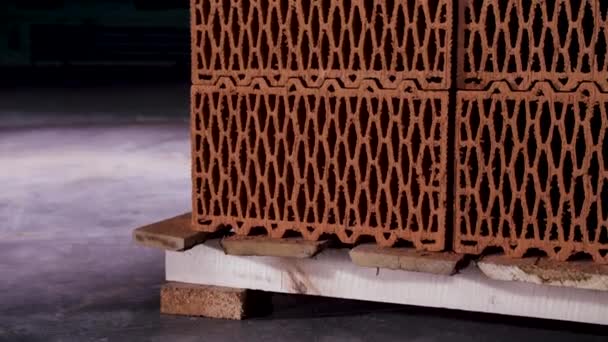 Κοντινό πλάνο σωρός από στοιβαγμένα πήλινα τούβλα με τρύπες τοποθετημένες σε ξύλινη παλέτα σε σκοτεινό αποθηκευτικό χώρο. Στικ. Κοντινό πλάνο των κεραμικών διάτρητων μπλοκ, έννοια των δομικών υλικών. — Αρχείο Βίντεο
