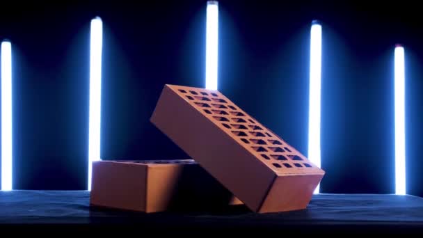 Gros plan de deux briques pleines de couleur rouge placées devant des lampes au néon sur fond noir. Images d'archives. Démonstration de matériaux de construction .