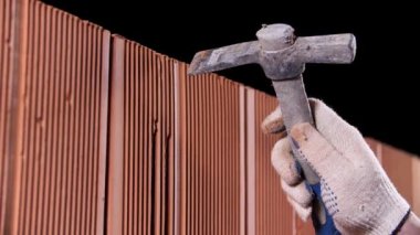 Çekiç tutan insan ellerine yakın çekim ve kara arka planda uzun bir delik açmak için kullanın. Stok görüntüleri. İnşaat işçisi tuğla duvarda bir çekiçle delik açıyor..