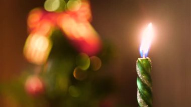 Noel arifesinde yanan güzel yeşil mum ve arka planda süslemeli Noel ağacı. Kavram. Yanan yeni yıl mumu, zaman aşımı etkisi.