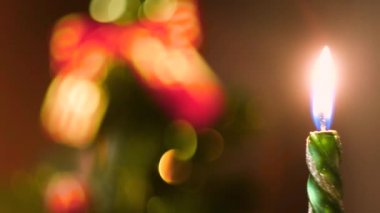 Noel arifesinde yanan güzel yeşil mum ve arka planda süslemeli Noel ağacı. Kavram. Yanan Yeni Yıl mumu.