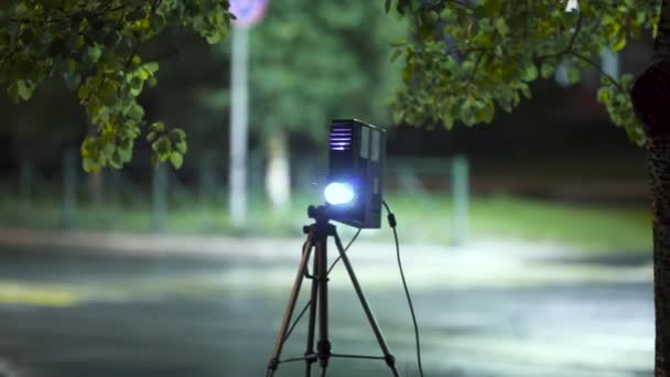 Projector lights beam for showing photo and video materials in the street at night on empty road background. Art. Video projector and tripod outdoors in the city. — Stock Video